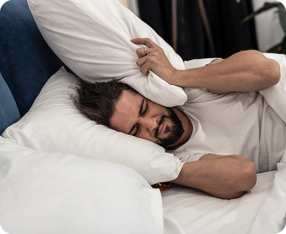 Man lying in bed struggling with sleep, tossing and turning due to breathing difficulties, wearing white shirt on white bedding in a dimly lit bedroom