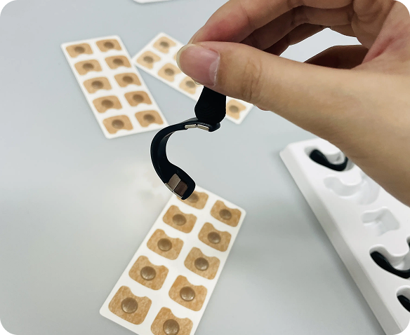 Close-up of hands applying white nasal breathing strips from a beige perforated strip sheet, demonstrating the easy application process of the medical breathing aid device
